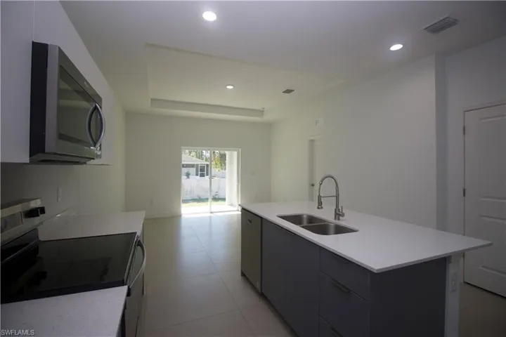 Kitchen with sink, electric range oven, a raised ceiling, a kitchen island with sink, and light tile patterned floors