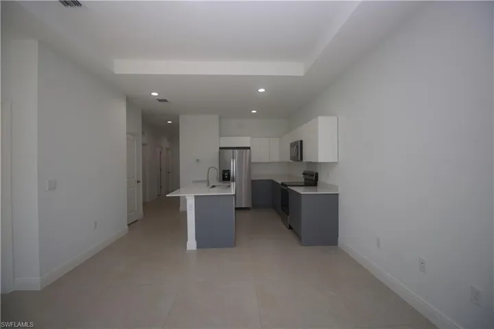 Kitchen with appliances with stainless steel finishes, a breakfast bar, sink, light tile patterned floors, and white cabinetry