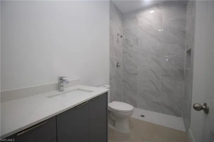 Bathroom with tiled shower, tile patterned flooring, vanity, and toilet