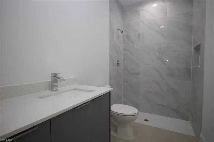 Bathroom with tiled shower, tile patterned flooring, vanity, and toilet