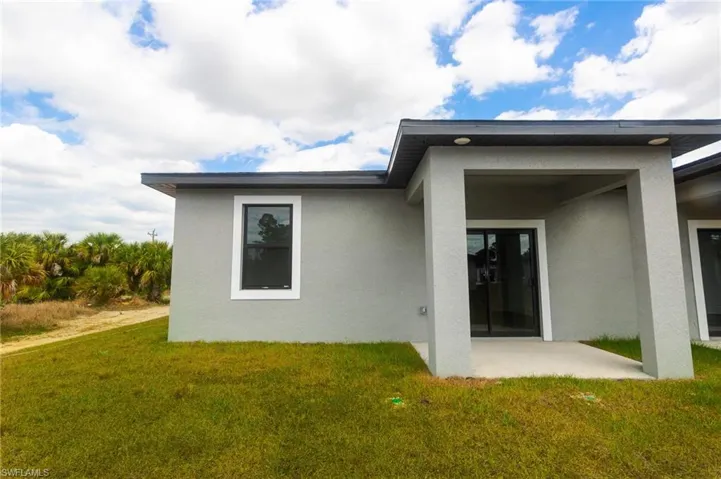 Back of house with stucco siding, a lawn, and a patio area
