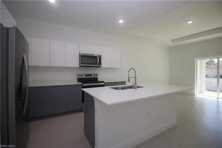 Kitchen featuring a kitchen island with sink, sink, white cabinets, and appliances with stainless steel finishes