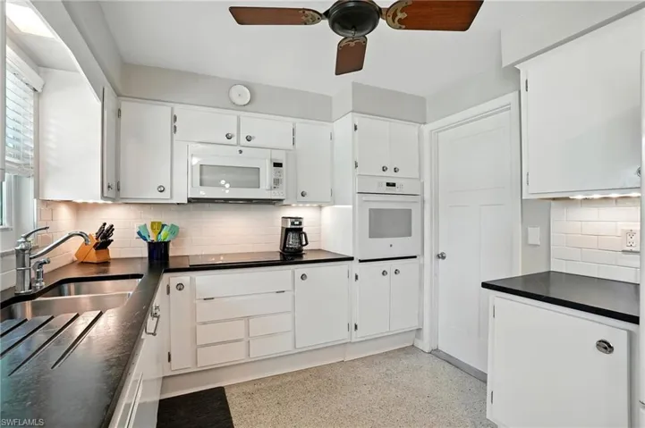 Kitchen featuring dark countertops, decorative backsplash, white appliances, ceiling fan, and white cabinets