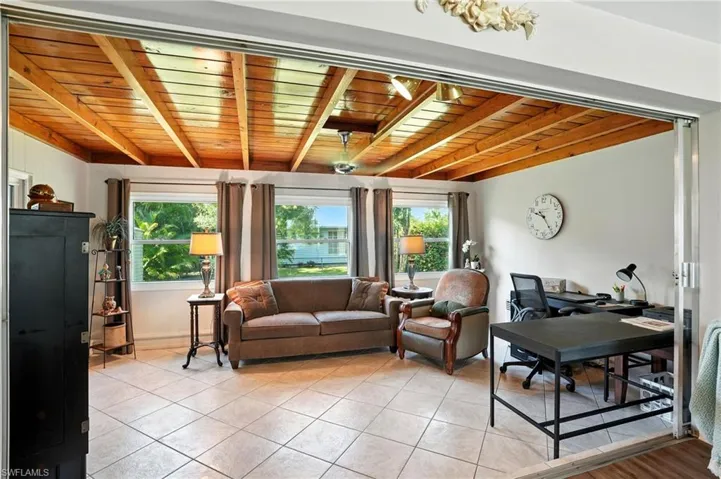 Living area with a wooden ceiling with exposed beams, an office area, and light tile patterned flooring