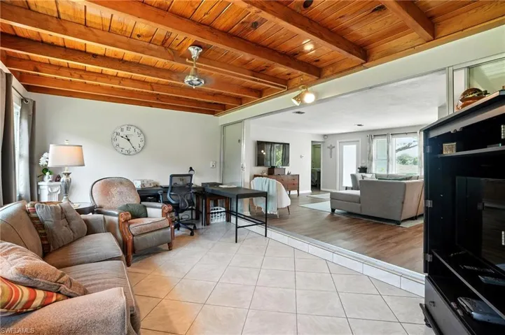 Living area featuring a wooden ceiling with exposed beams, light tile patterned floors, and a desk
