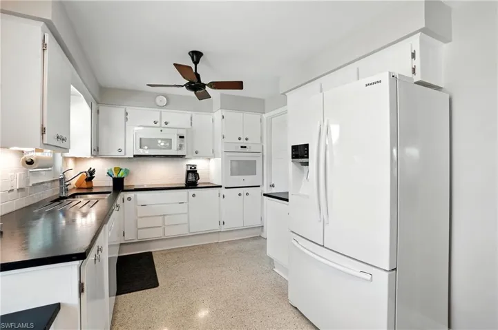 Kitchen with white appliances, dark countertops, decorative backsplash, dark speckled floor, and white cabinetry