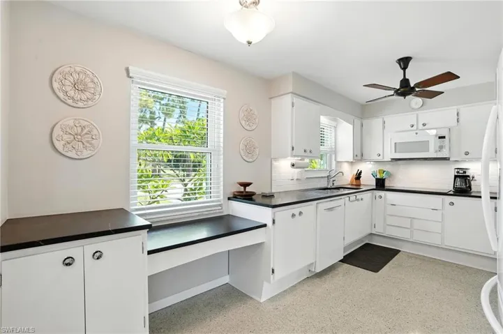Kitchen with white appliances, dark countertops, decorative backsplash, white cabinetry, and a ceiling fan