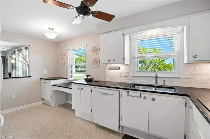 Kitchen featuring tasteful backsplash, dark countertops, a ceiling fan, white cabinets, and dark aggregate flooring