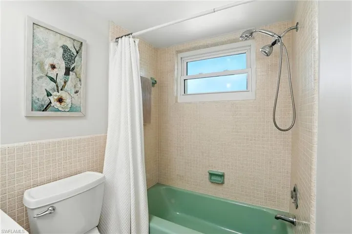 Full bath with tile walls, shower / tub combo with curtain, and a wainscoted wall