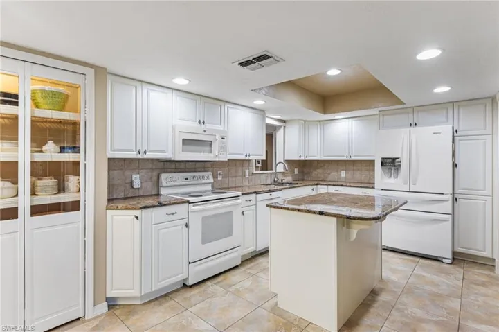 Kitchen with white appliances, decorative backsplash, dark stone countertops, white cabinets, and recessed lighting