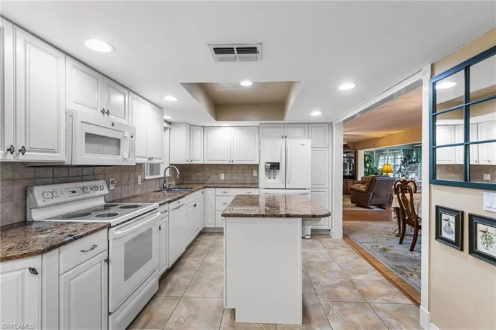 Kitchen featuring white appliances, dark stone countertops, white cabinets, a center island, and recessed lighting