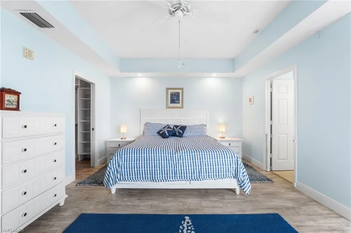 Bedroom with wood finished floors, a raised ceiling, a walk in closet, and a ceiling fan