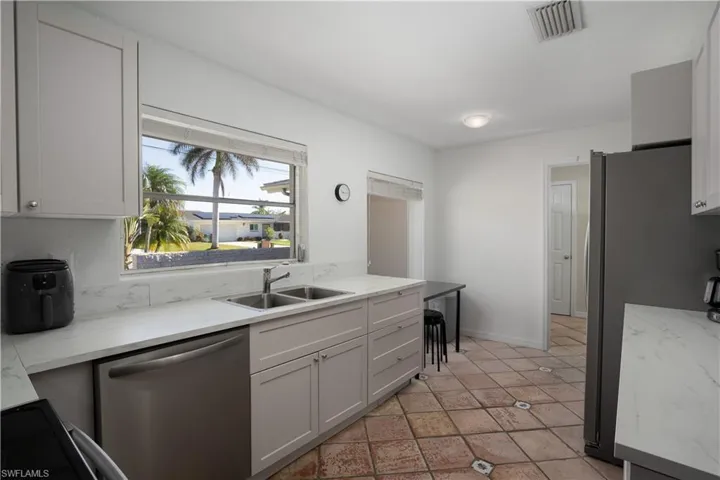 Kitchen featuring white cabinets, sink, light stone countertops, light tile patterned floors, and stainless steel appliances