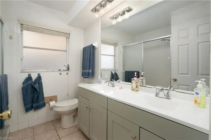 Bathroom with walk in shower, tile patterned floors, toilet, vanity, and tile walls