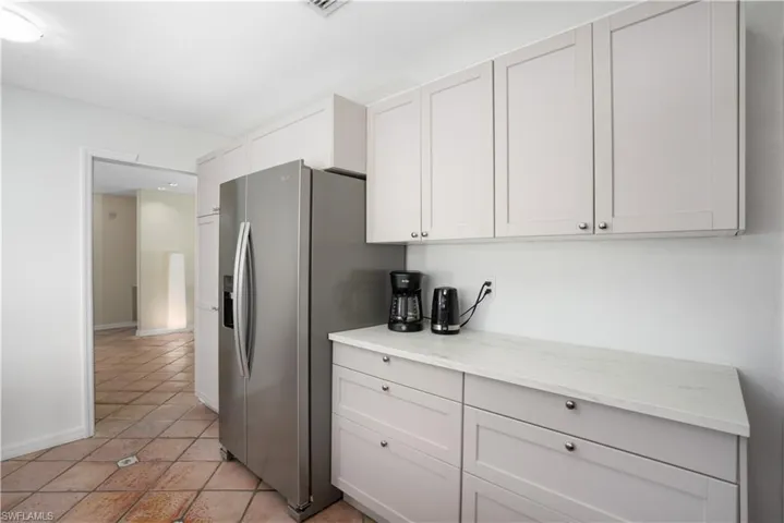 Kitchen featuring light stone countertops, stainless steel refrigerator with ice dispenser, and white cabinetry