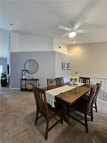 Dining area featuring light carpet, vaulted ceiling, and a ceiling fan