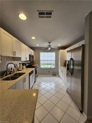 Kitchen with white cabinets, light tile patterned floors, stainless steel appliances, light stone countertops, and recessed lighting