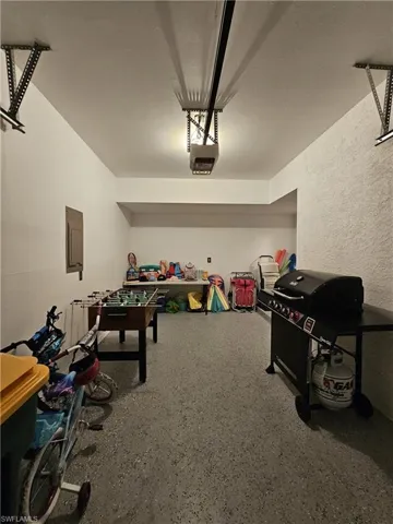 Rec room featuring a garage, a textured wall, a textured ceiling, electric panel, and dark aggregate flooring