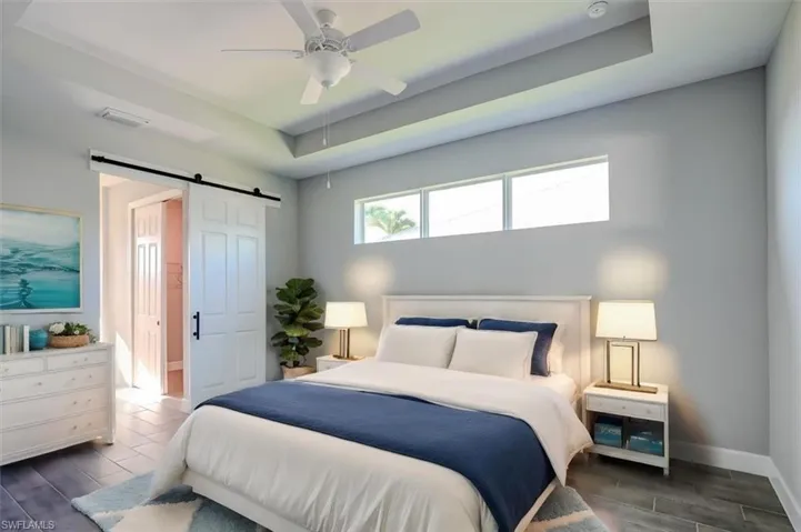 Bedroom featuring a barn door, dark hardwood / wood-style floors, ceiling fan, and a raised ceiling