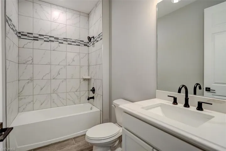 Full bathroom featuring tiled shower / bath, vanity with extensive cabinet space, toilet, and wood-type flooring