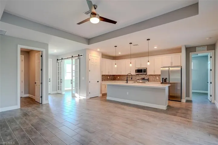 Kitchen featuring stainless steel appliances, hanging light fixtures, ceiling fan, a kitchen island with sink, and a barn door