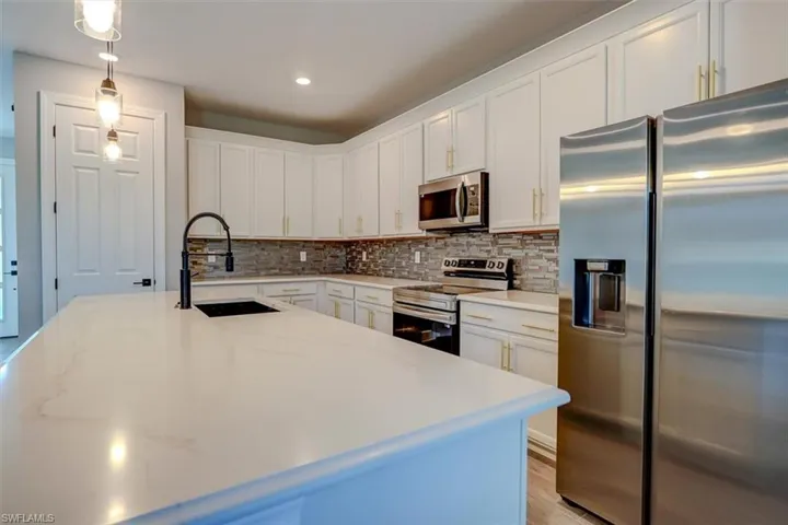 Kitchen with white cabinets, backsplash, appliances with stainless steel finishes, sink, and pendant lighting