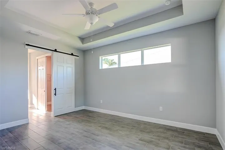 Unfurnished room with a barn door, wood-type flooring, ceiling fan, and a raised ceiling