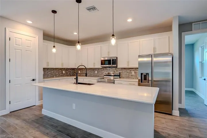 Kitchen featuring tasteful backsplash, white cabinetry, an island with sink, appliances with stainless steel finishes, and sink