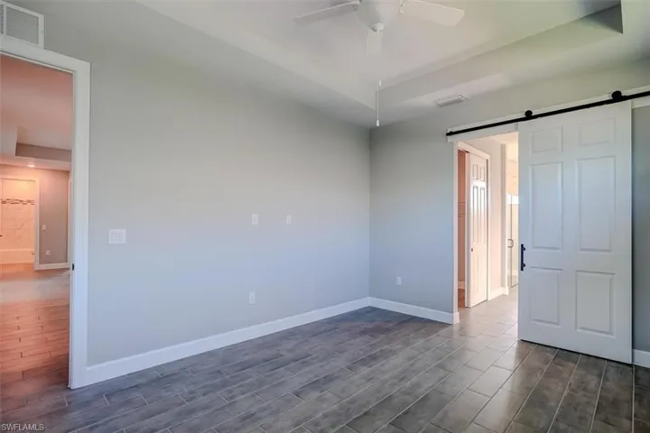 Unfurnished bedroom with a barn door, dark hardwood / wood-style floors, and ceiling fan