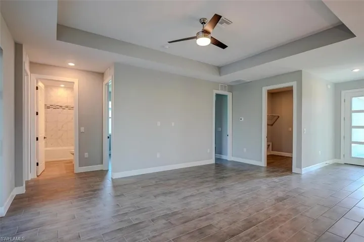Unfurnished bedroom with ensuite bathroom, a tray ceiling, ceiling fan, hardwood / wood-style floors, and a walk in closet