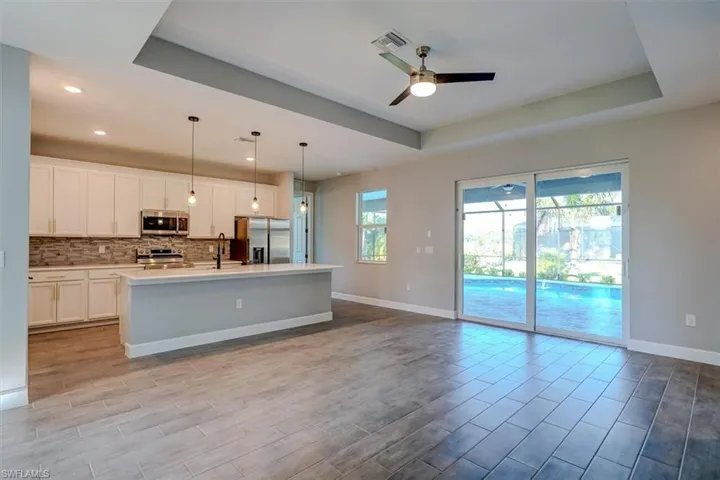 Kitchen featuring stainless steel appliances, a kitchen island with sink, decorative light fixtures, ceiling fan, and a raised ceiling