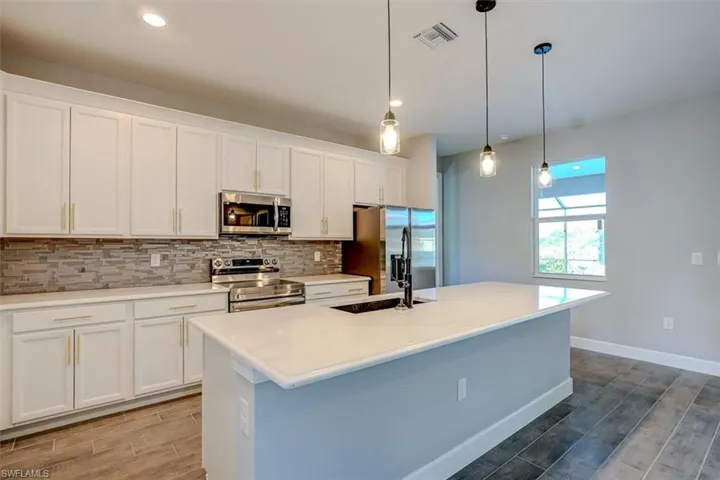 Kitchen with stainless steel appliances, white cabinets, a kitchen island with sink, pendant lighting, and tasteful backsplash