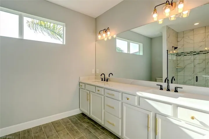 Bathroom featuring walk in shower, plenty of natural light, large vanity, and double sink