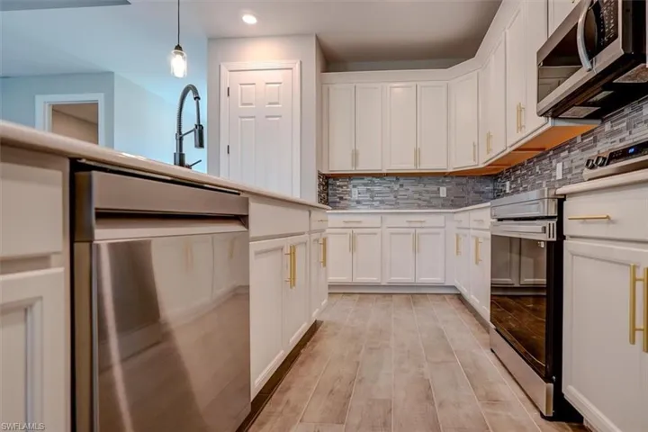 Kitchen featuring light hardwood / wood-style flooring, backsplash, pendant lighting, and appliances with stainless steel finishes