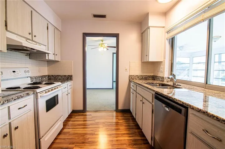 Kitchen with white electric range oven, stainless steel dishwasher, dark stone counters, light wood finished floors, and ceiling fan