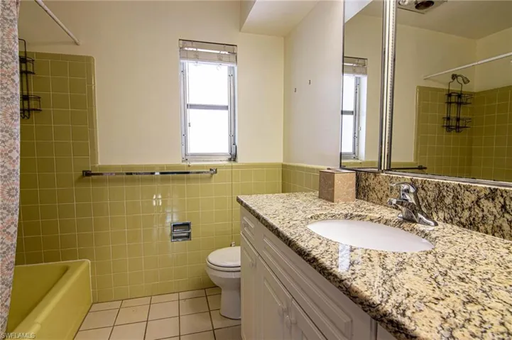 Full bathroom with vanity, tiled shower / bath combo, light tile patterned flooring, tile walls, and a wainscoted wall