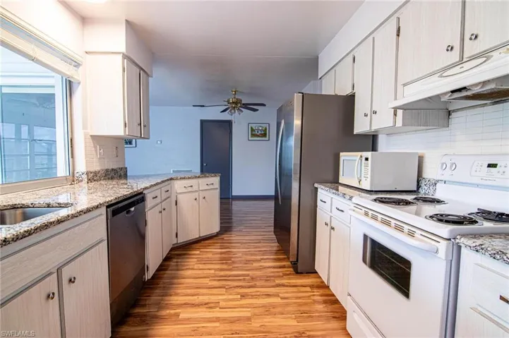 Kitchen featuring white appliances, light stone counters, light wood finished floors, tasteful backsplash, and a ceiling fan
