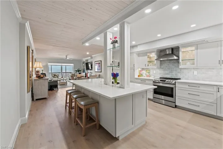 Kitchen featuring white cabinetry, stainless steel electric range oven, wall chimney range hood, decorative backsplash, and a kitchen island