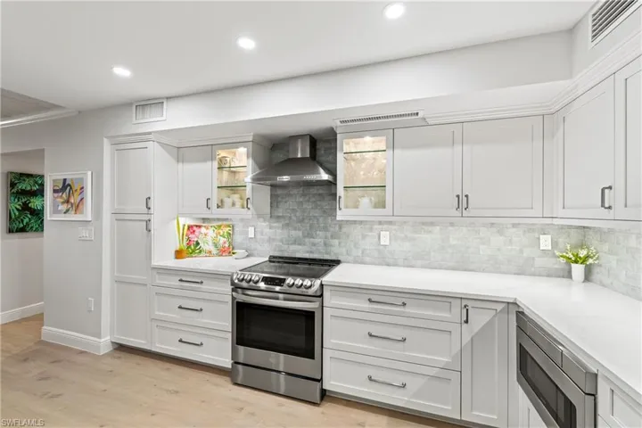 Kitchen with white cabinets, light hardwood / wood-style floors, wall chimney range hood, and stainless steel appliances