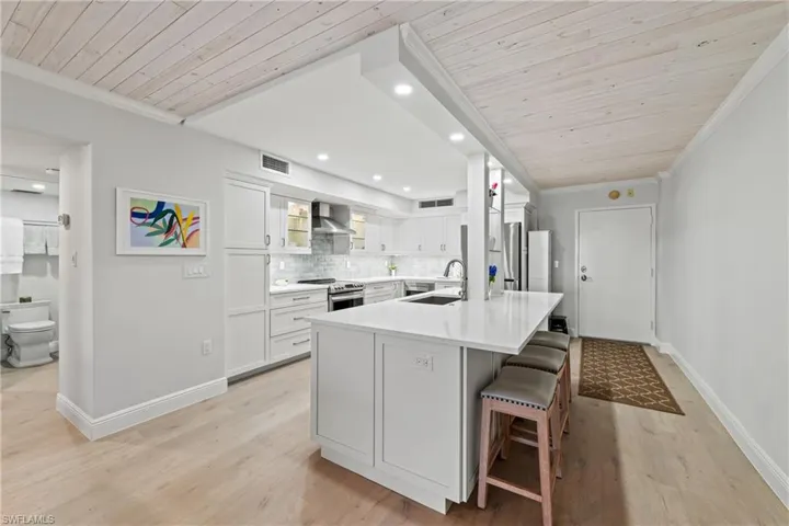 Kitchen with tasteful backsplash, wall chimney exhaust hood, wood ceiling, a kitchen island with sink, and white cabinets