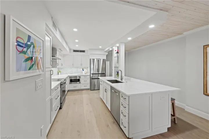 Kitchen with sink, decorative backsplash, appliances with stainless steel finishes, white cabinetry, and wood ceiling