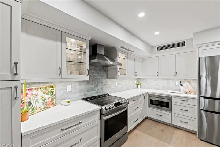 Kitchen featuring appliances with stainless steel finishes, white cabinetry, and wall chimney exhaust hood