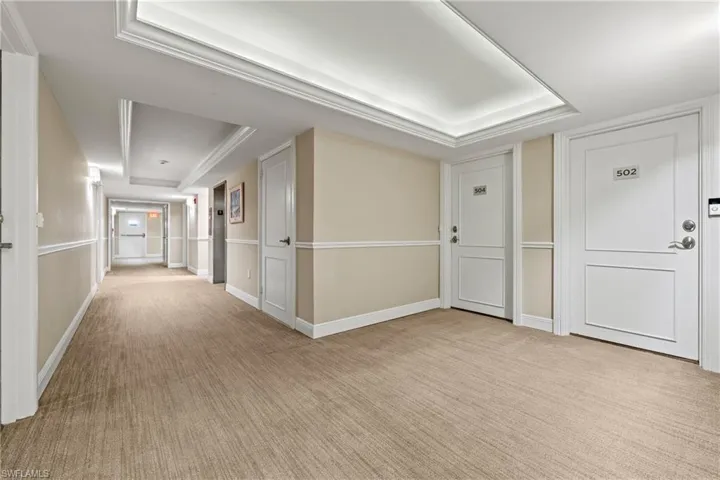 Hallway featuring a raised ceiling and light carpet