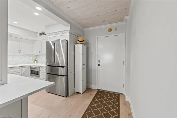 Kitchen with white cabinets, crown molding, light hardwood / wood-style flooring, decorative backsplash, and stainless steel fridge