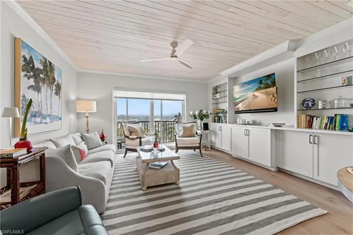 Living room featuring crown molding, light hardwood / wood-style flooring, built in shelves, ceiling fan, and wood ceiling