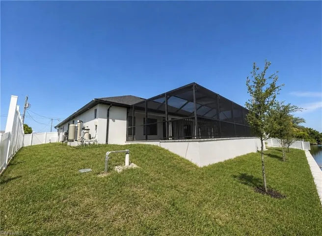 Screened lanai, white stucco exterior, black asphalt shingle roof, white vinyl privacy fence, waterside setting