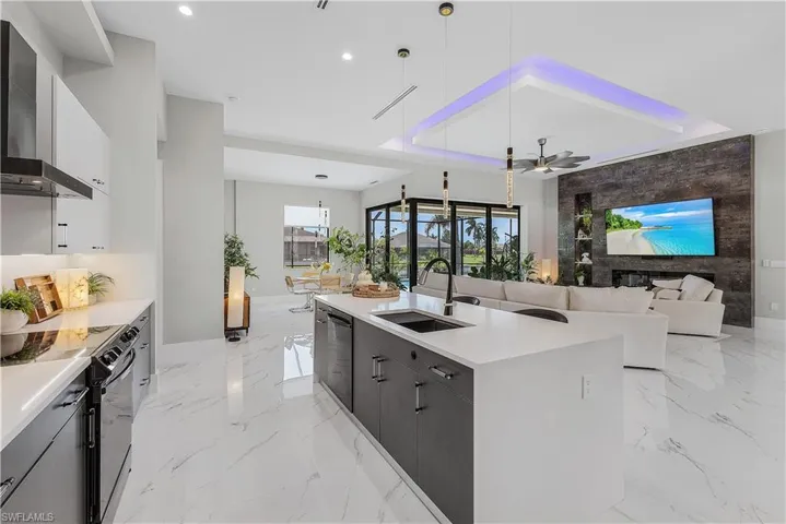 Kitchen with wall chimney exhaust hood, sink, black / electric stove, light tile patterned floors, and hanging light fixtures
