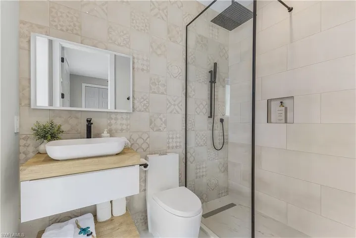 Bathroom featuring tiled shower, toilet, vanity, and tile walls