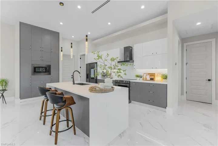 Kitchen with hanging light fixtures, light tile patterned floors, stainless steel appliances, a center island with sink, and wall chimney range hood