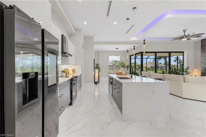 Kitchen with stainless steel appliances, wall chimney exhaust hood, a center island with sink, pendant lighting, and light tile patterned flooring